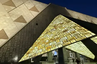大埃及博物館入口的三角形天窗，金色光線灑在刻滿象形文字的巨大石牆上