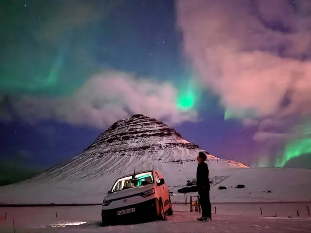 綠色極光與紫紅色雲層籠罩草帽山，雪地前方有一個仰望天空的人影